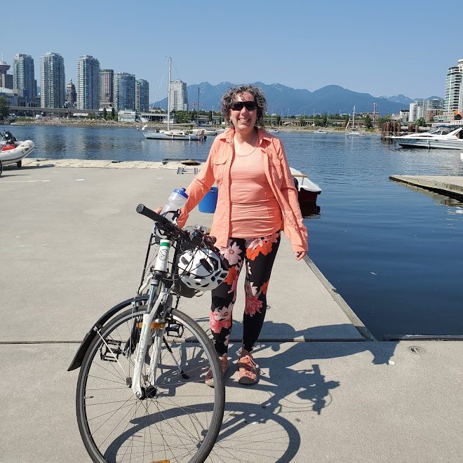 Celia standing with a bicycle by the water at Creekside